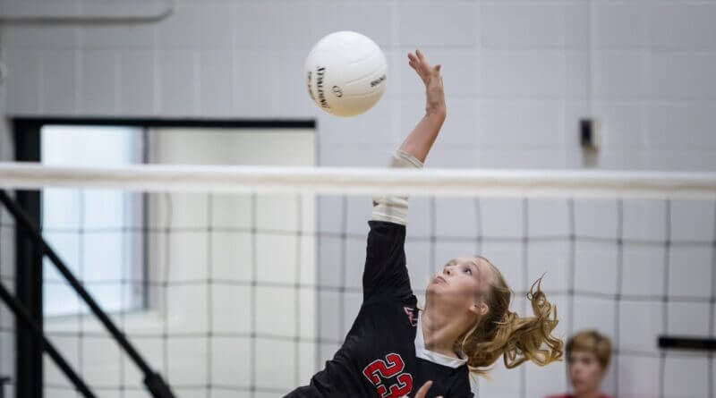 A volleyball player reaches above the net to play the ball during a high school match.